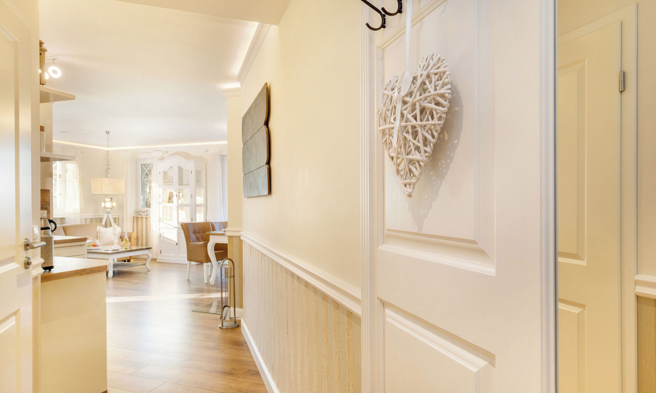 A hallway with a dining area, a white wall with a decorative piece, and a door with a handle.