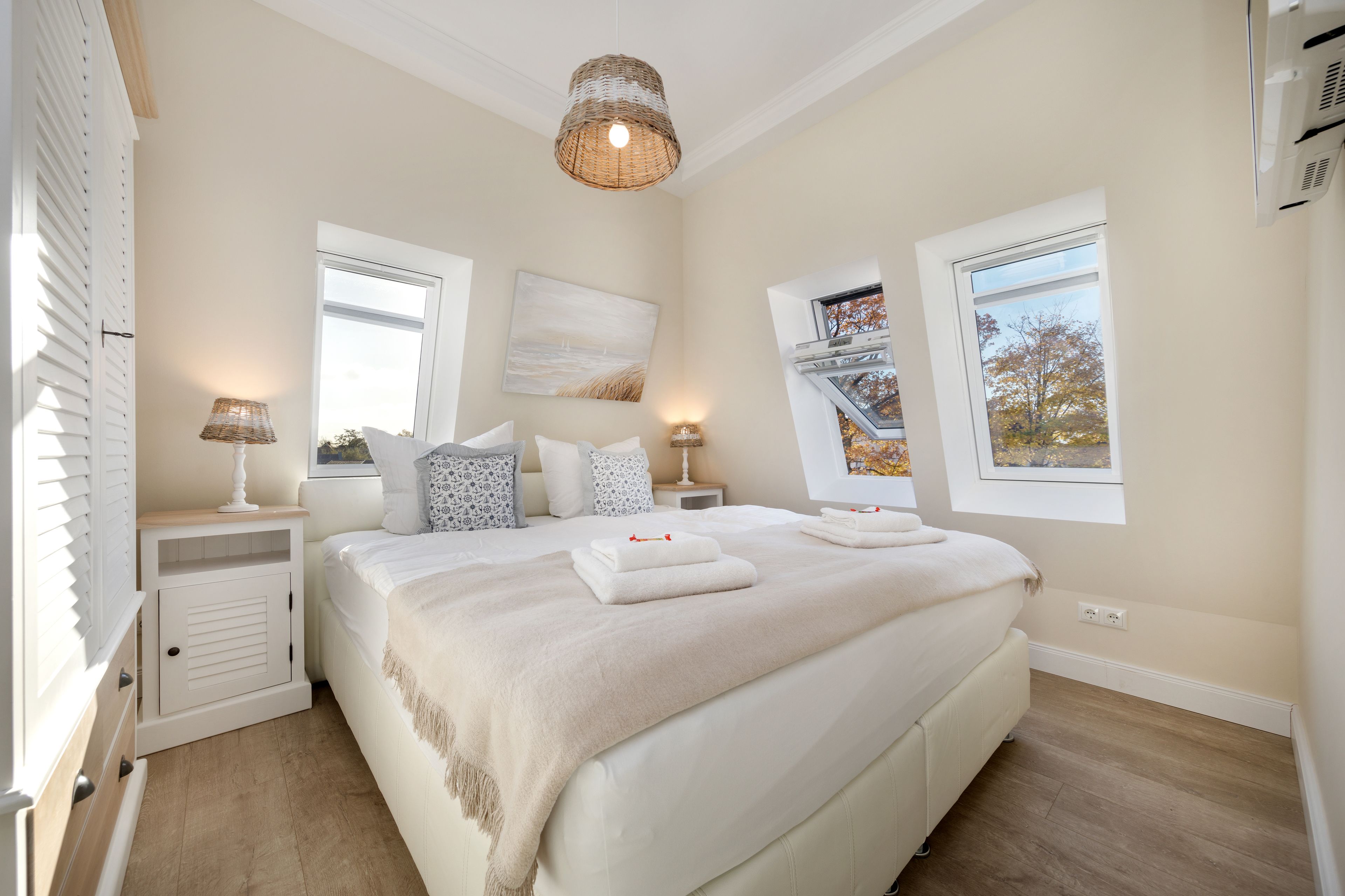 Une chambre avec un grand lit, deux tables de chevet, une lampe suspendue et deux fenêtres.