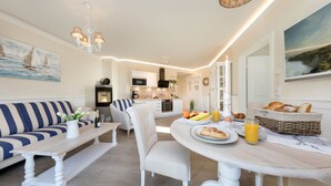 Una cocina moderna con armarios blancos, una zona de comedor con una mesa redonda, y un sofá con cojines a rayas.