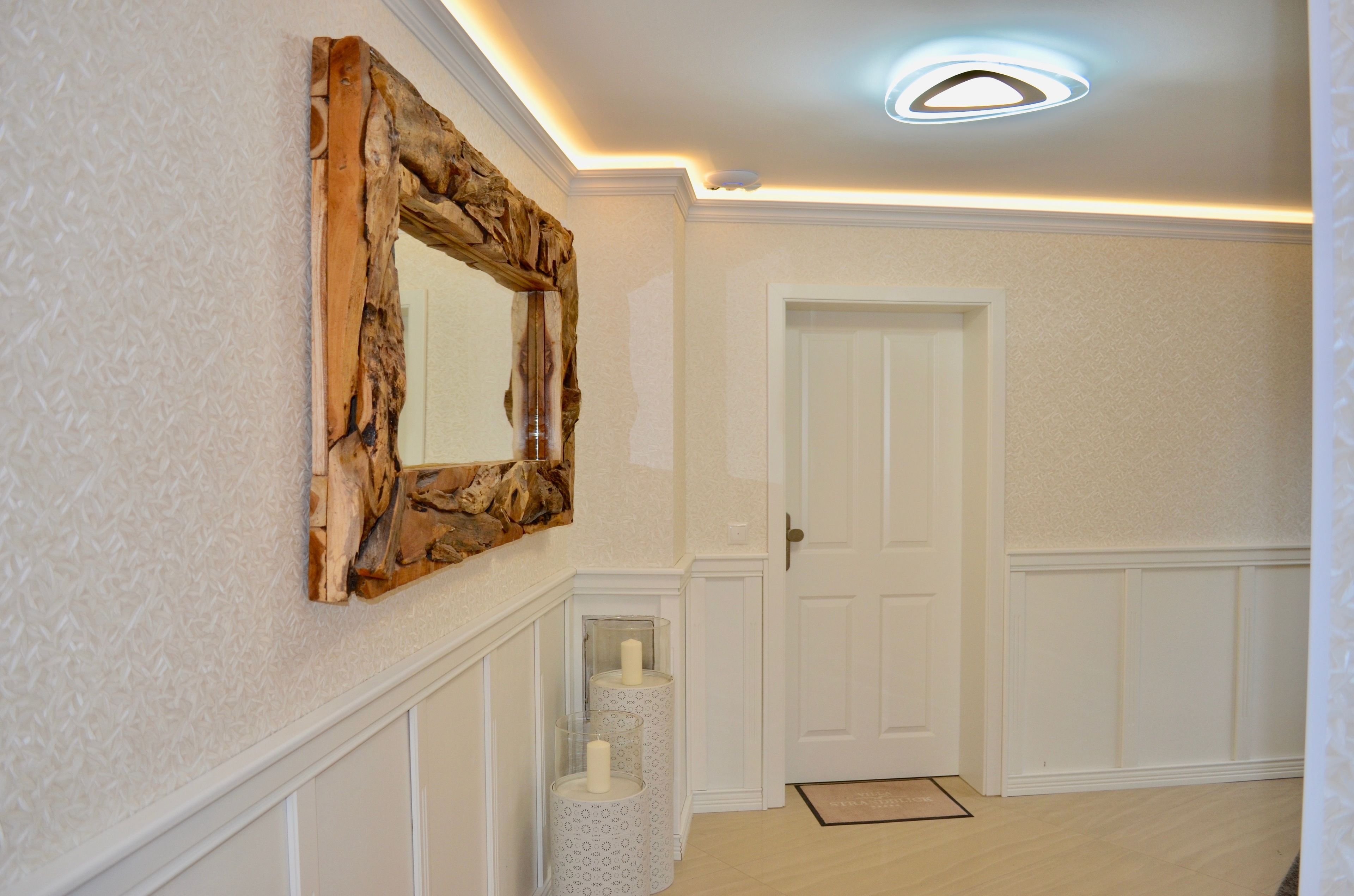 Un corridoio con uno specchio con cornice in legno, una porta bianca e una parete decorata.