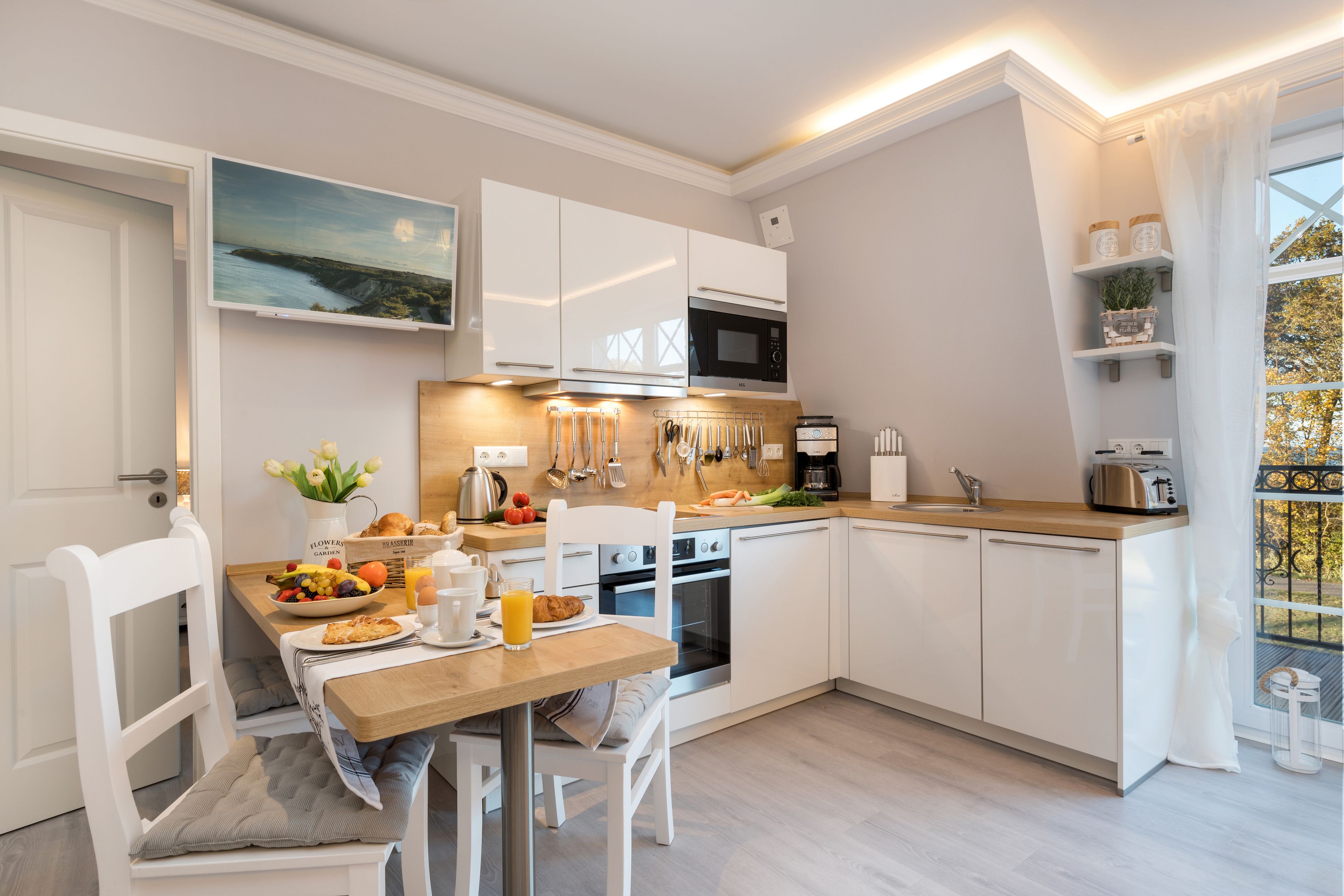 A modern kitchen with white cabinetry, a wooden countertop, and a dining area with a table and chairs.