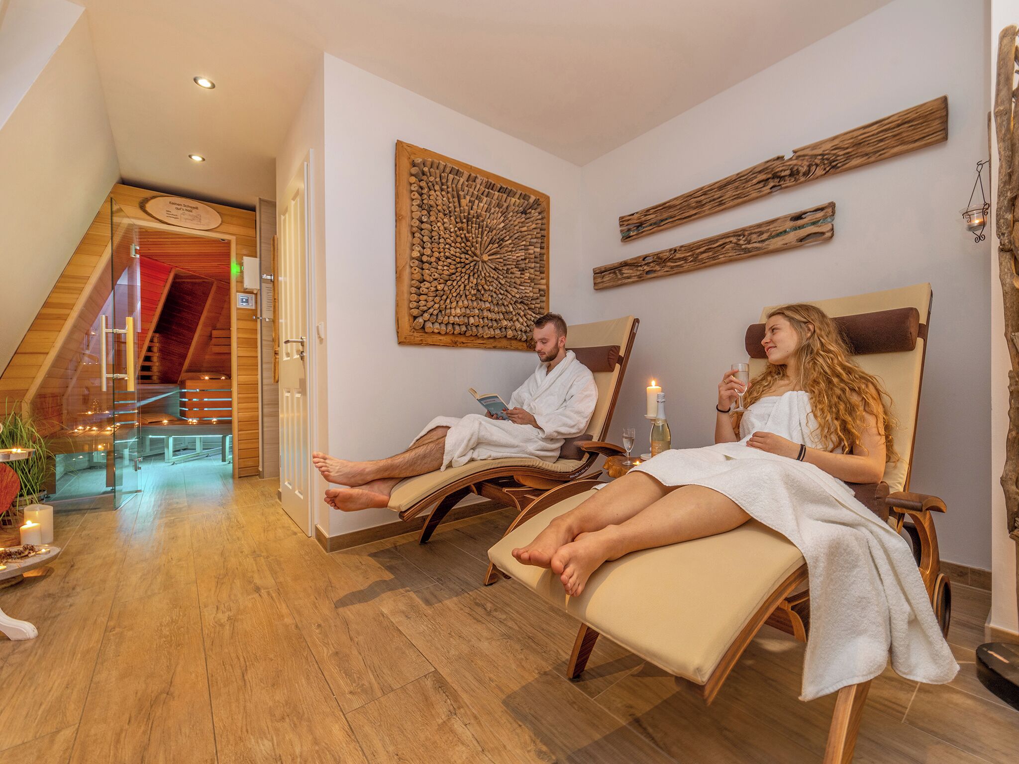 A spa room with two reclining chairs, a wooden floor, a large wall art piece, and a staircase in the background.