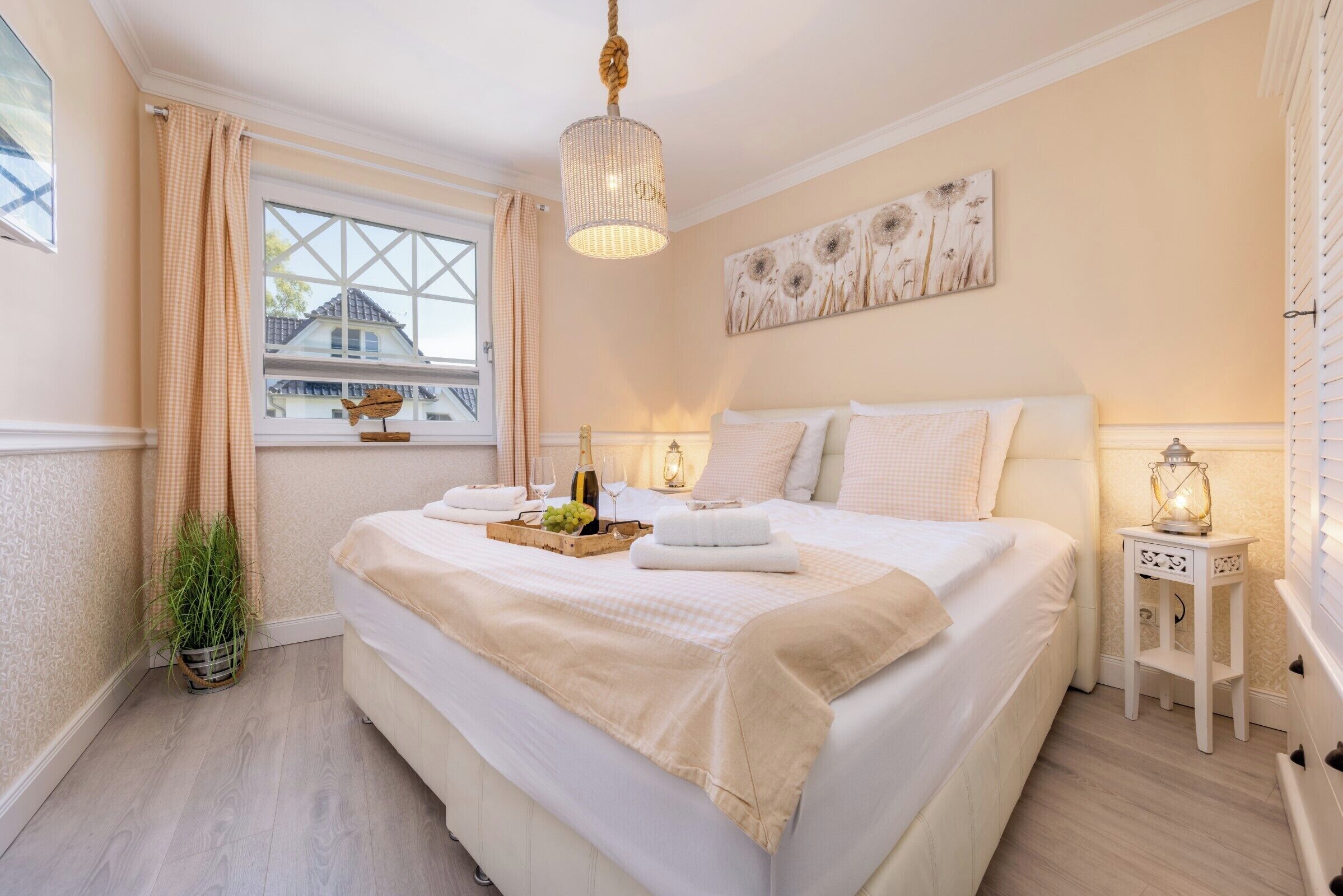 Un dormitorio ordenado con una cama grande, lámparas de noche, una ventana con cortinas y una obra de arte colgada en la pared.
