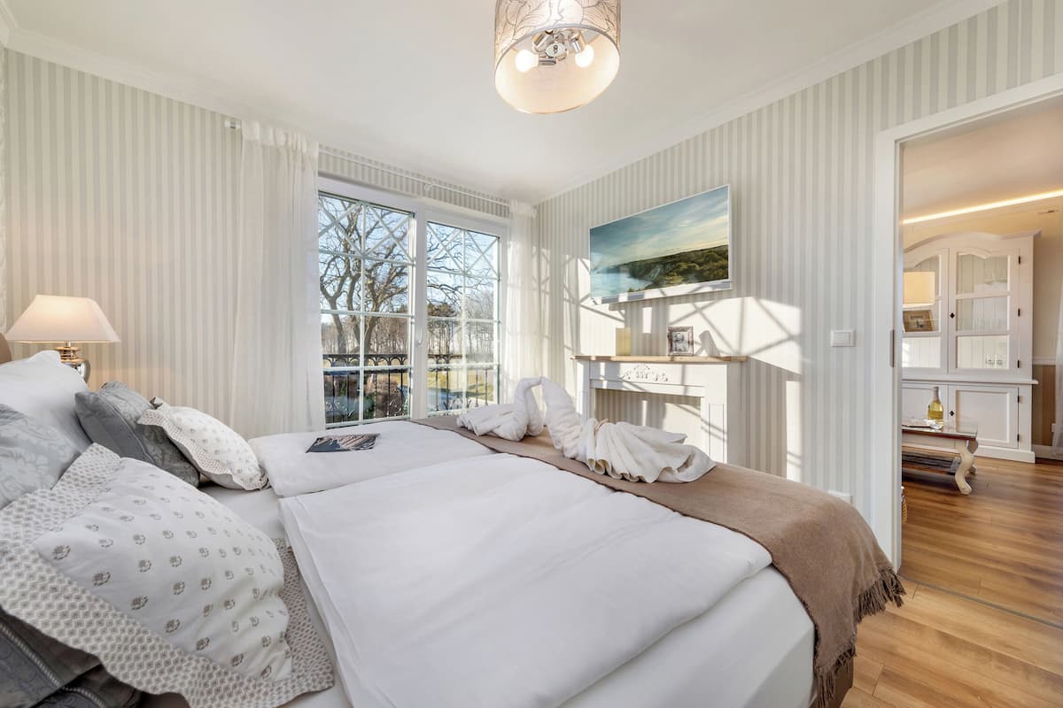 A spacious bedroom with a large bed, a bedside table with a lamp, and a view of a balcony.