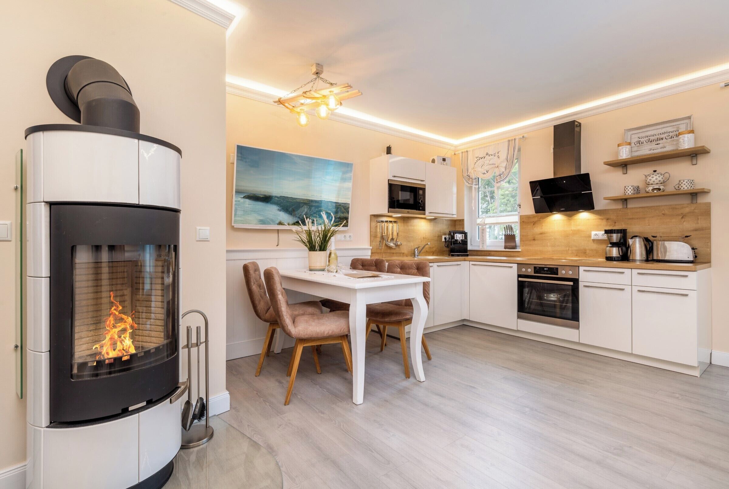 A modern kitchen with a built-in stove, white cabinets, a dining table with chairs, and a large painting on the wall.