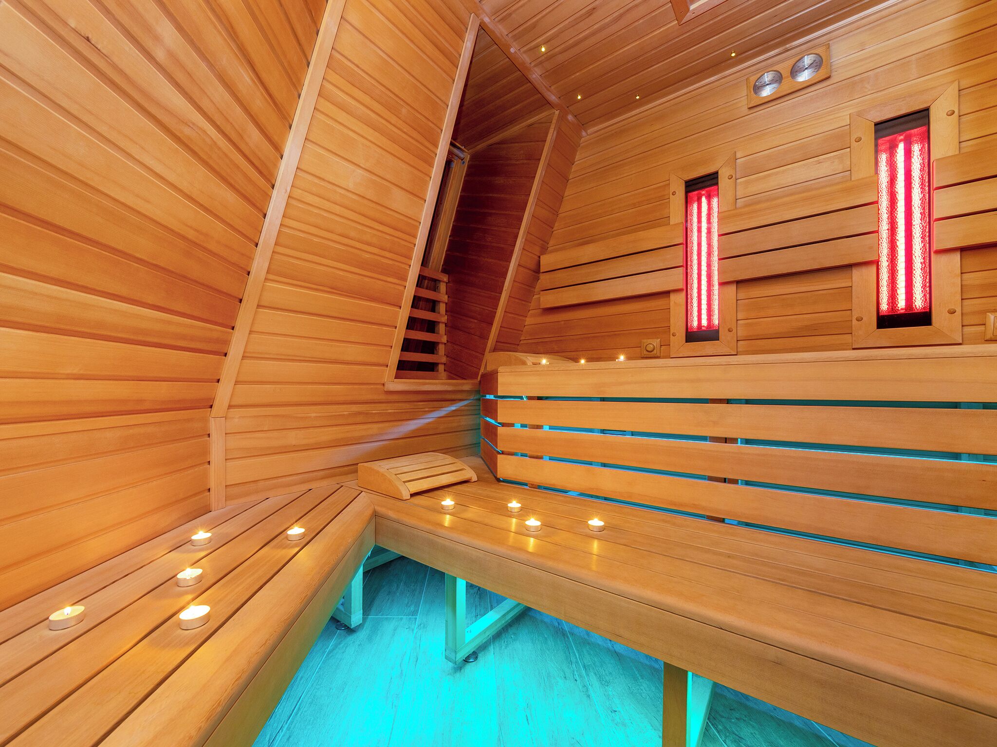 A sauna with wooden benches and benches, a wooden ceiling, and a small window with red light.