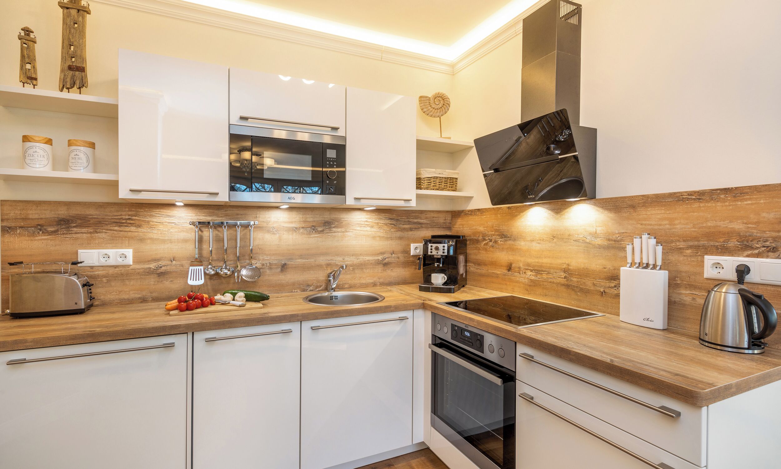 A modern kitchen with white cabinets, wooden countertops, a built-in oven, a coffee machine, and a kettle.