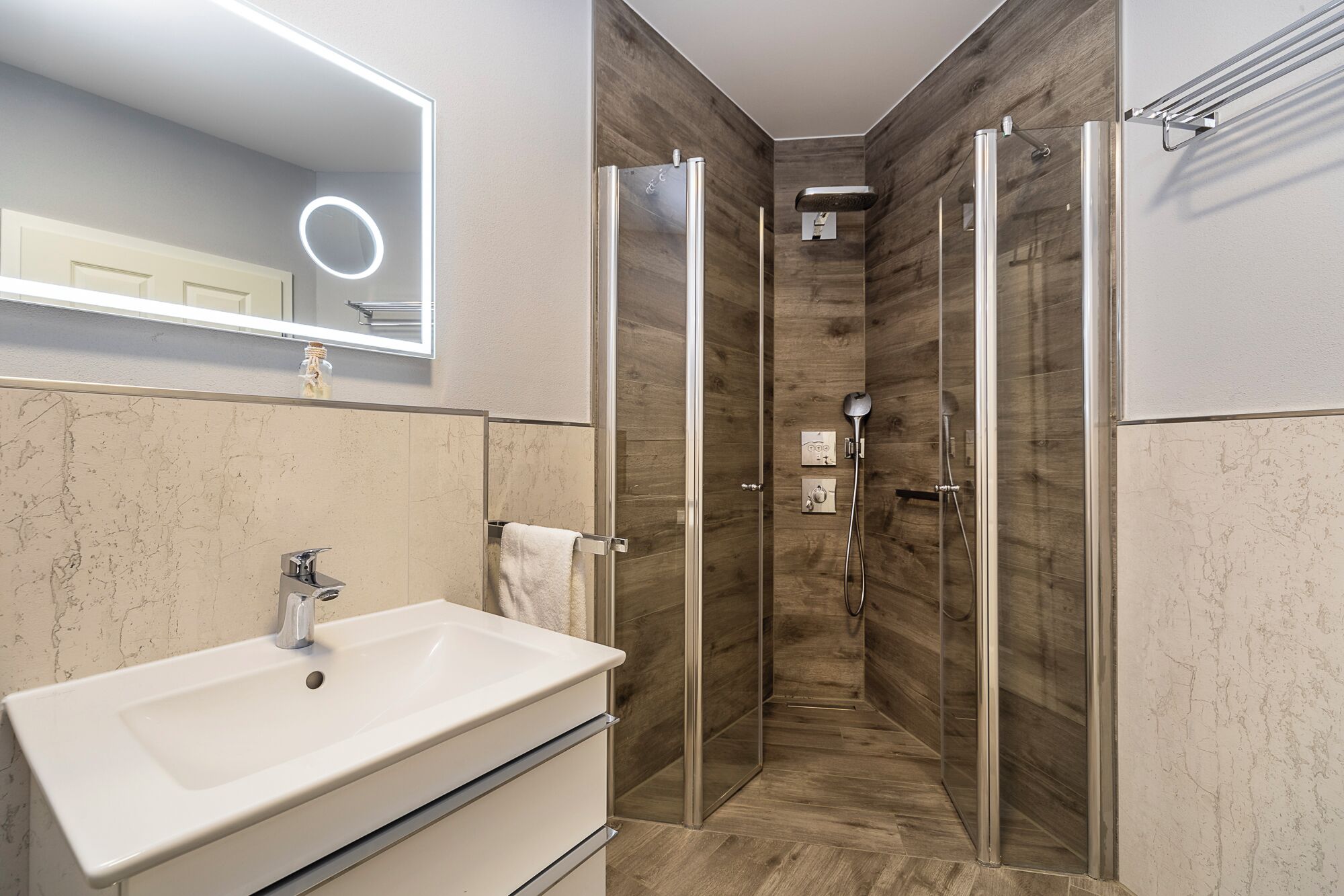 Une salle de bain moderne dotée d’un grand lavabo, d’un miroir avec un anneau lumineux et d’une douche à l’italienne.