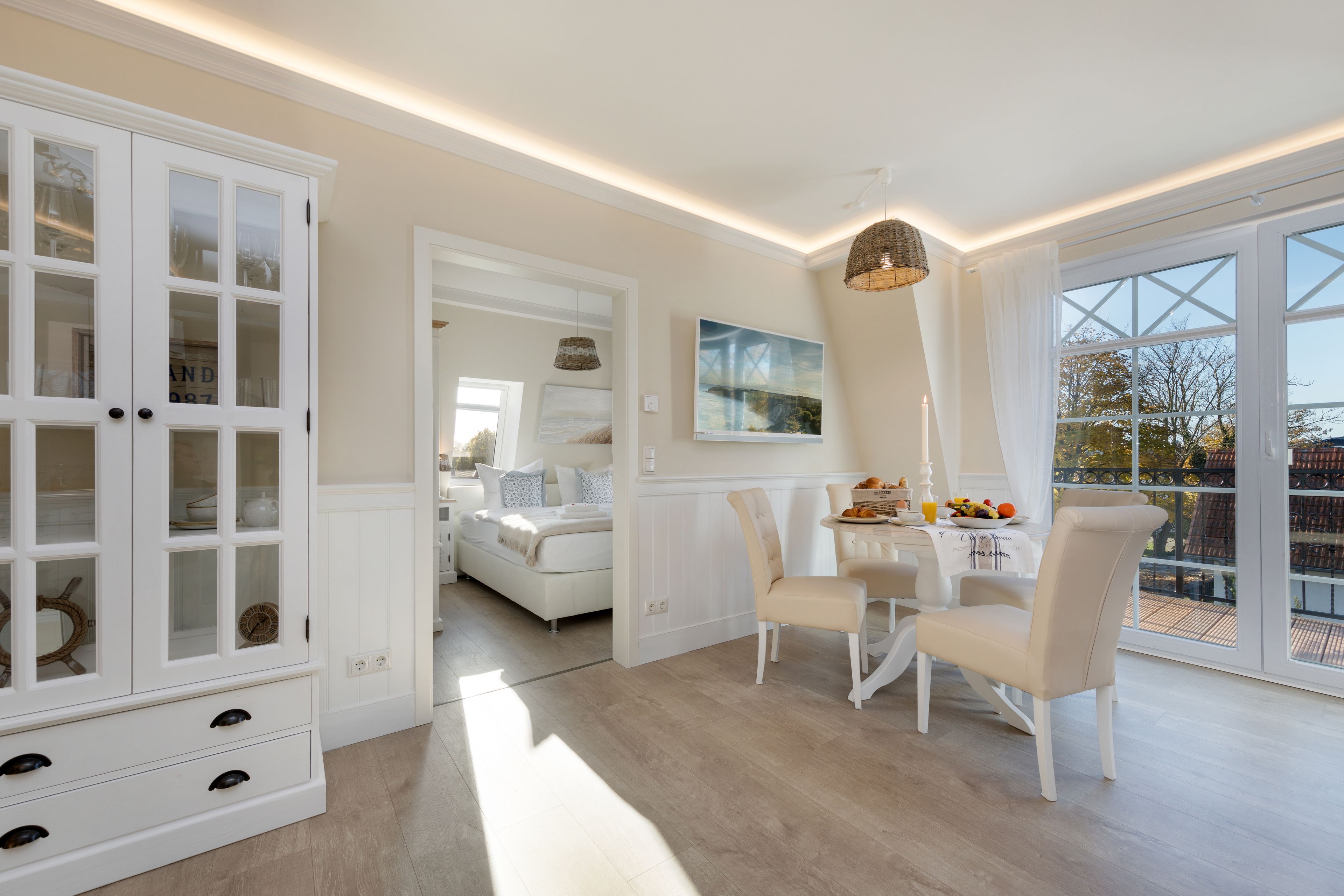 Un espacio amplio con zona de comedor, un armario blanco con puertas de cristal y un ventanal que ofrece vistas al exterior.