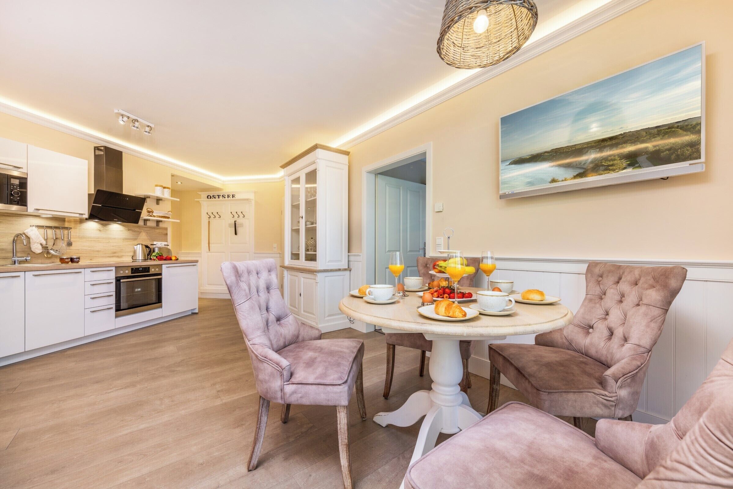 A modern kitchen with white cabinetry, a dining area with a round table, and a large window.