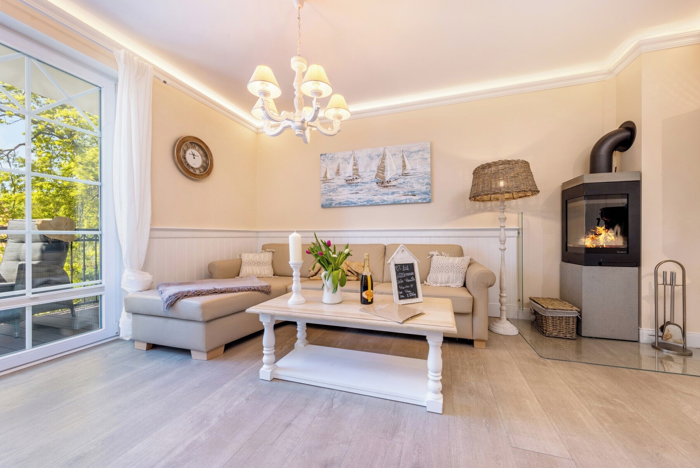 Una sala de estar acogedora con un sofá blanco, una mesita de centro blanca, una chimenea y un amplio ventanal con cortinas.