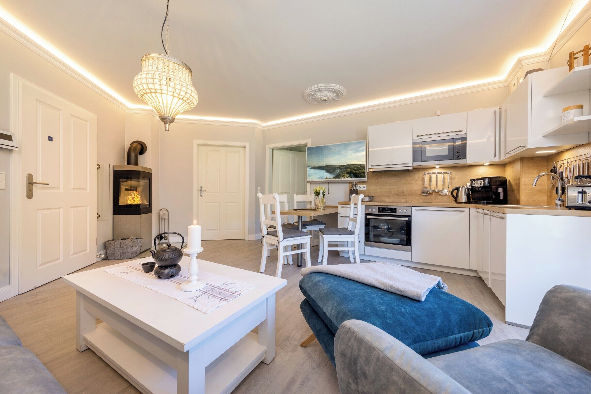 Una cocina moderna con armarios blancos, un comedor con mesa y sillas, y una sala de estar con sofá y mesa de centro.