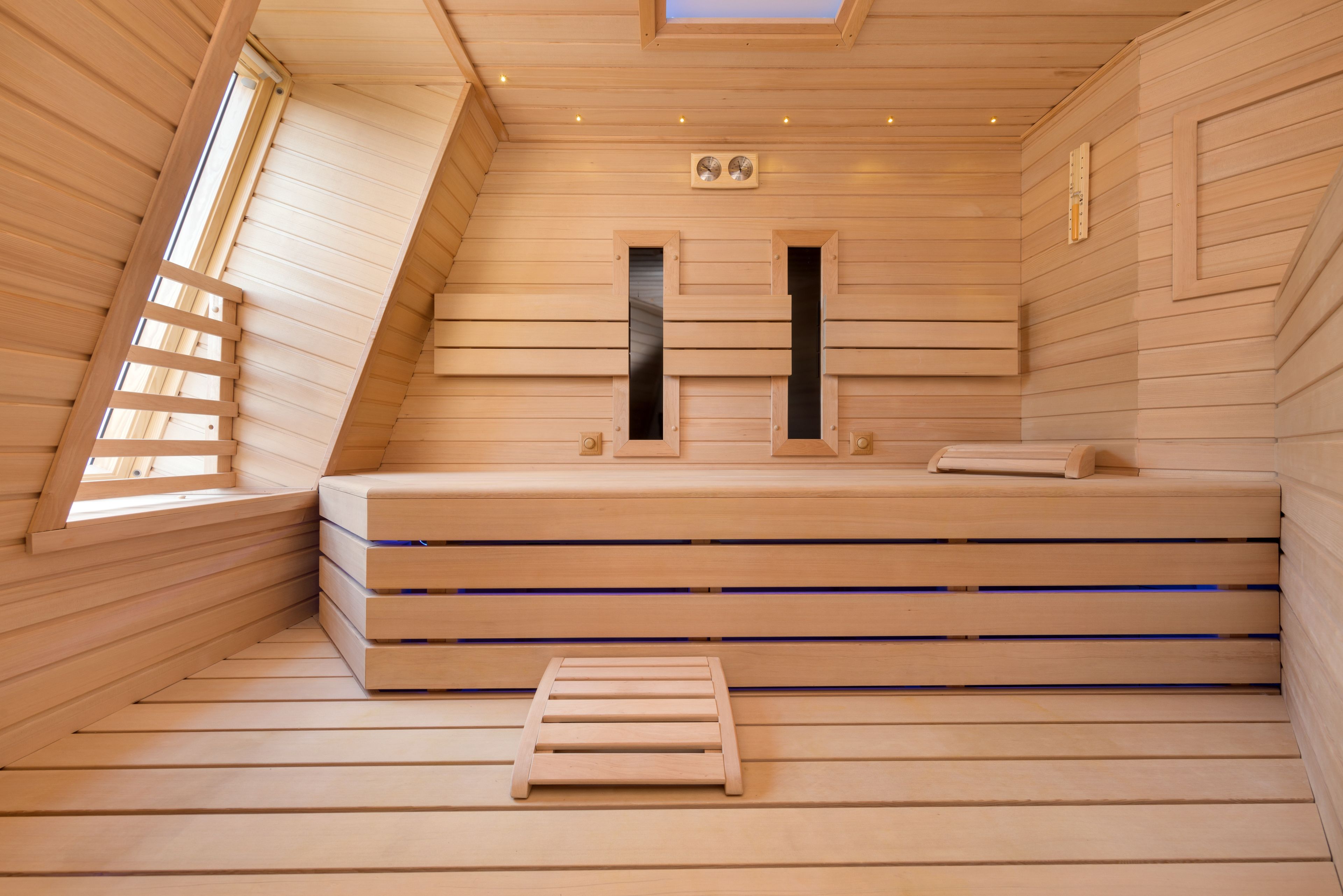 A wooden sauna with benches, a skylight, and a small window.