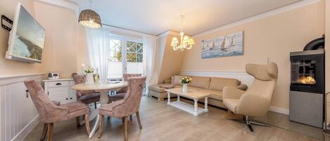 Een woonkamer met een eethoek, beige banken, een salontafel, een open haard en kunstwerken aan de wanden.