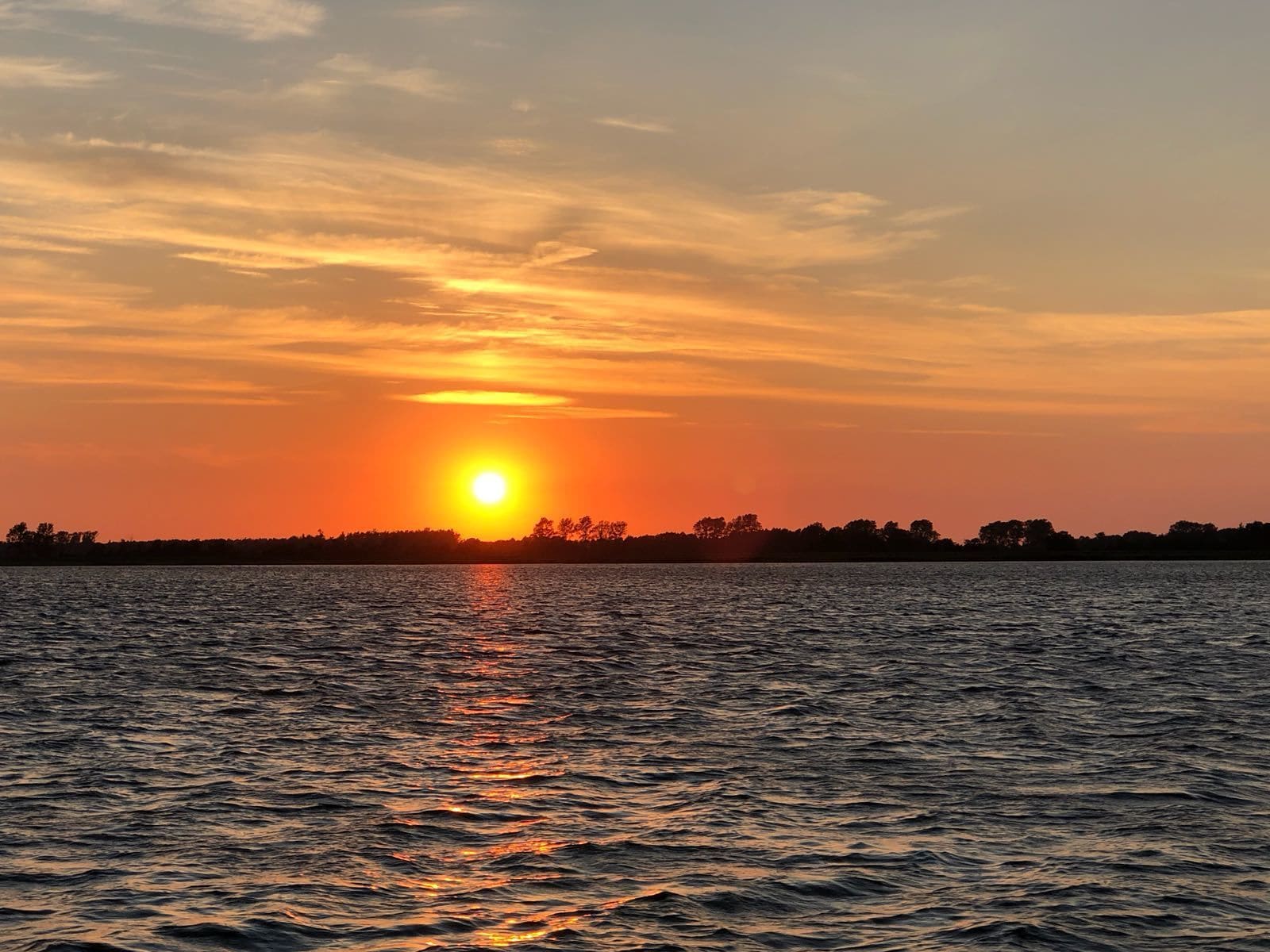 A sunset over a calm body of water with a silhouette of trees in the distance.