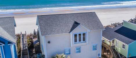 A beachfront property with a two-story house, a covered porch, and a small pool.