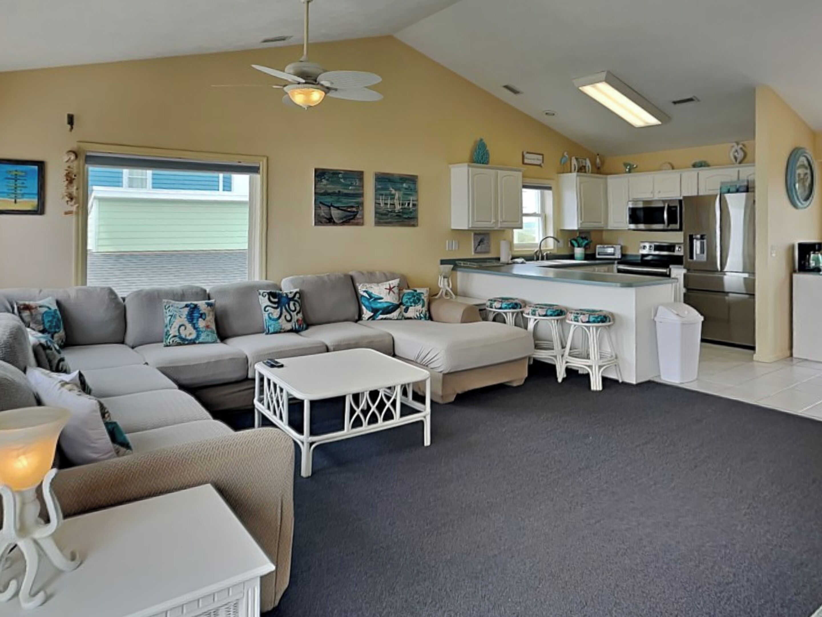 A modern living room with a sectional sofa, a small coffee table, and a kitchen area with white cabinets and stainless steel appliances.