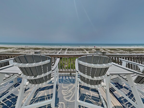 Vista a la playa desde una terraza con dos sillas y un tapete estampado.