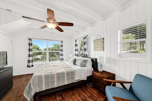 A bedroom with a bed, a ceiling fan, a window with blinds, a dresser, and a chair.