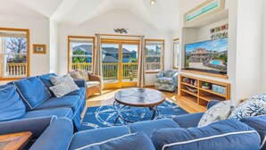 Ein großzügiger Wohnraum mit einer blauen Sofagarnitur, einem runden Couchtisch und einem Fernseher auf einem Holzboden.