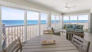 A spacious balcony with a view of the beach and ocean, furnished with a table, chairs, and a sofa. - Sparkling Views from this two bedroom, two bathroom Gulf Front Sandy Bend 8 (Sanibel)