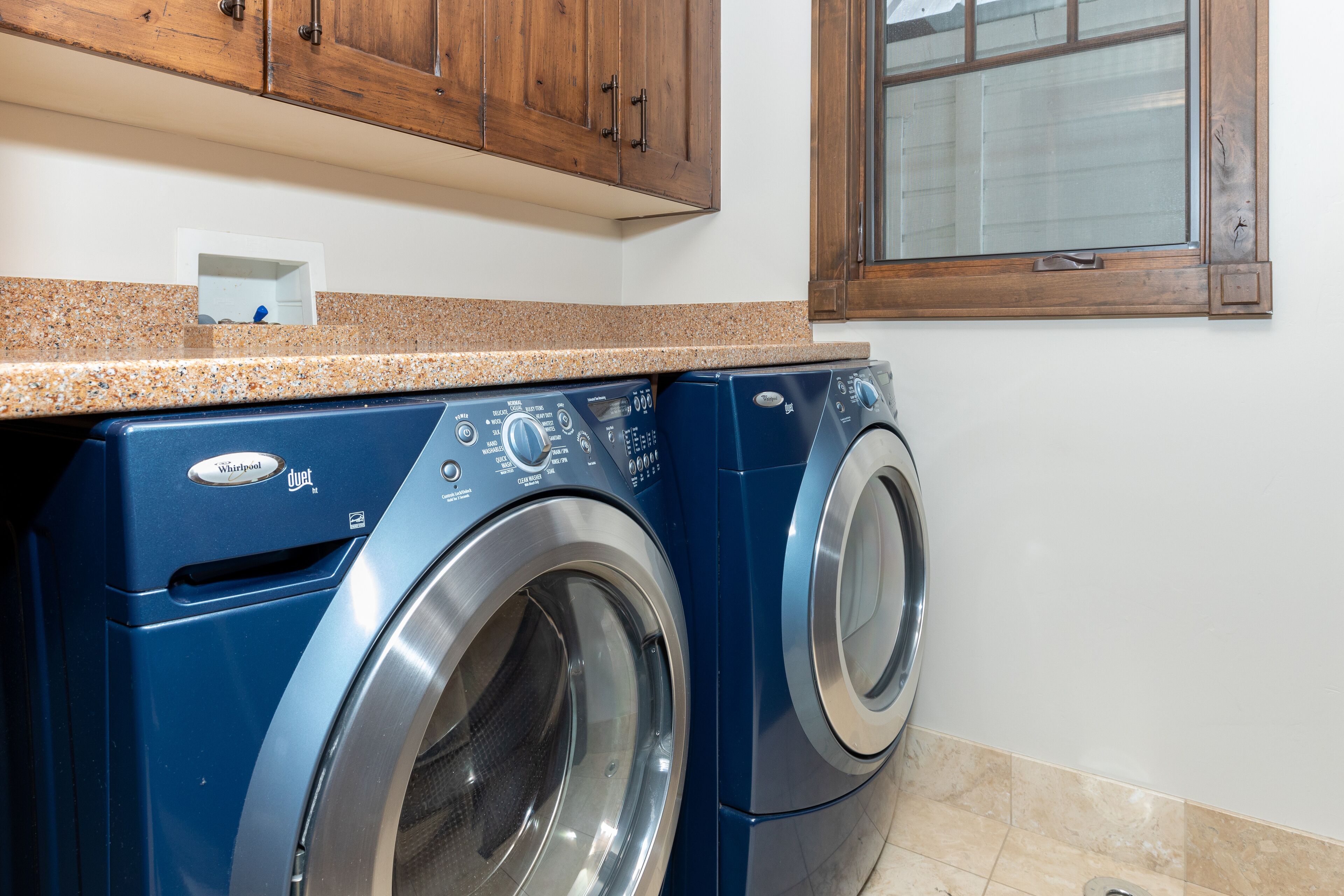 Un lave-linge à chargement frontal dans une cuisine avec des meubles en bois et une fenêtre au-dessus.