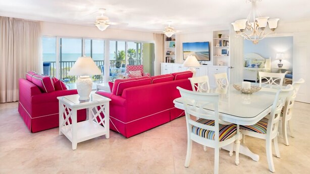 A spacious living room with a red sofa, white coffee table, and a glass dining table with chairs.