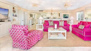 A spacious living room with a large sofa set, a television, and a kitchen in the background.