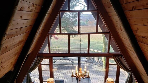 A cozy room with a large window, wooden walls, a cushioned seating area, and a chandelier. - Private Cabin with Lake & Mountain Views on 10 Acres - Near Resorts - Book Now! (Champion)