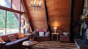 A cozy cabin interior with a wooden ceiling, a fireplace, a sofa, a coffee table, and a chandelier. - Private Cabin with Lake & Mountain Views on 10 Acres - Near Resorts - Book Now! (Champion)