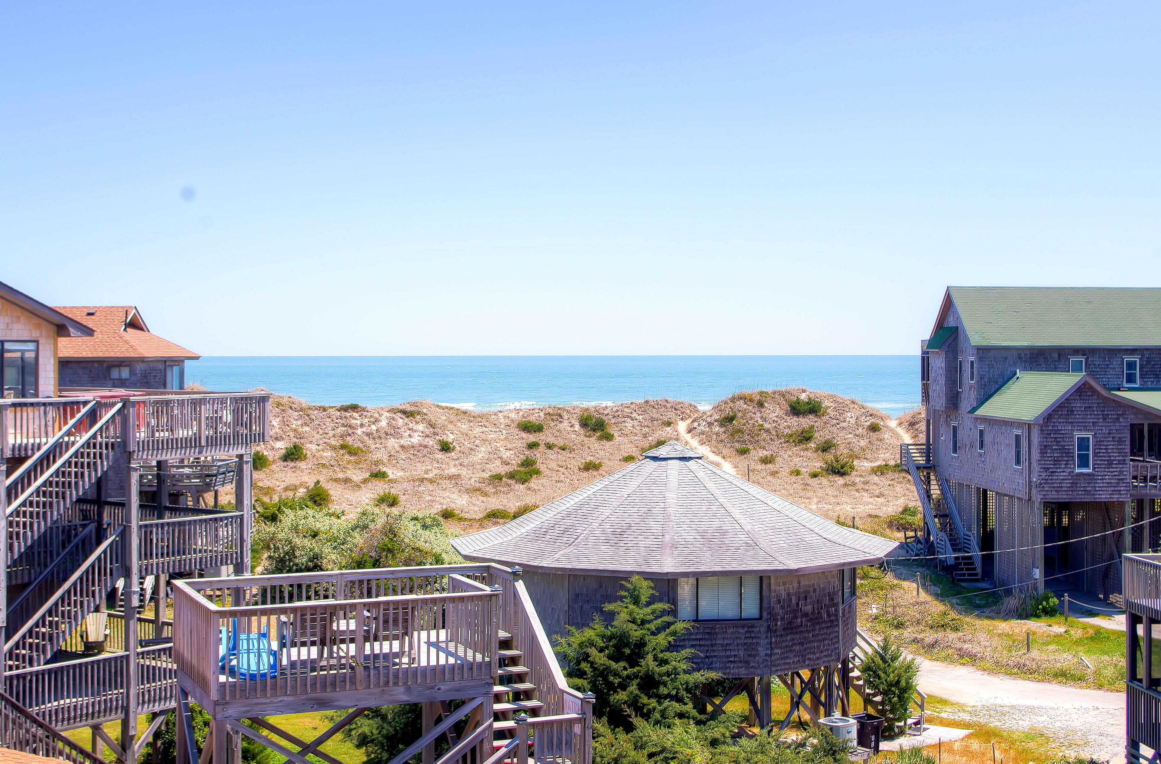 Ein Ferienhaus direkt am Strand mit einer Holzterrasse, einem Pavillon und einem Haus mit grüner Dachbegrünung.