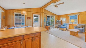 A spacious living area with wooden paneling, a large wooden dining table, and a cozy seating arrangement. - Oceanview Dog Friendly Home in Avon w/ Grill, Games. Only 3 Lots From Beach! (Avon)