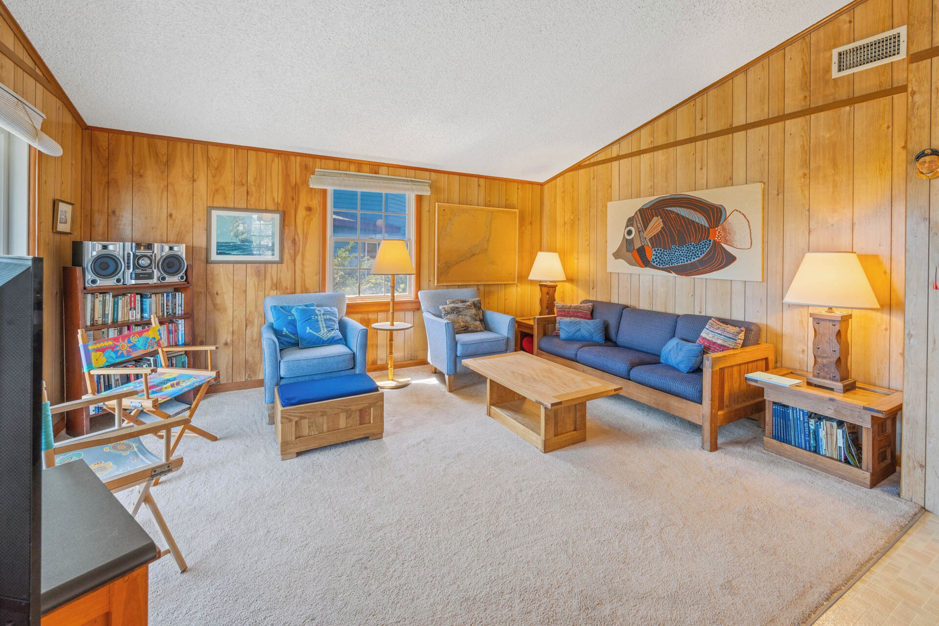 A cozy living room with wooden walls, a bookshelf, a blue armchair, a sofa, and two lamps.