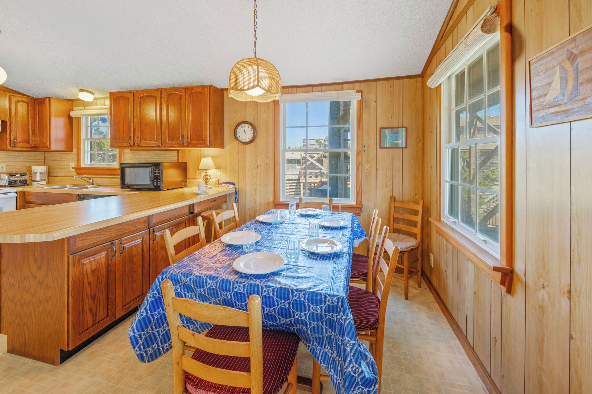 Une cuisine avec des meubles en bois, un four à micro-ondes et une table à manger dressée pour six personnes, recouverte de nappes bleues.