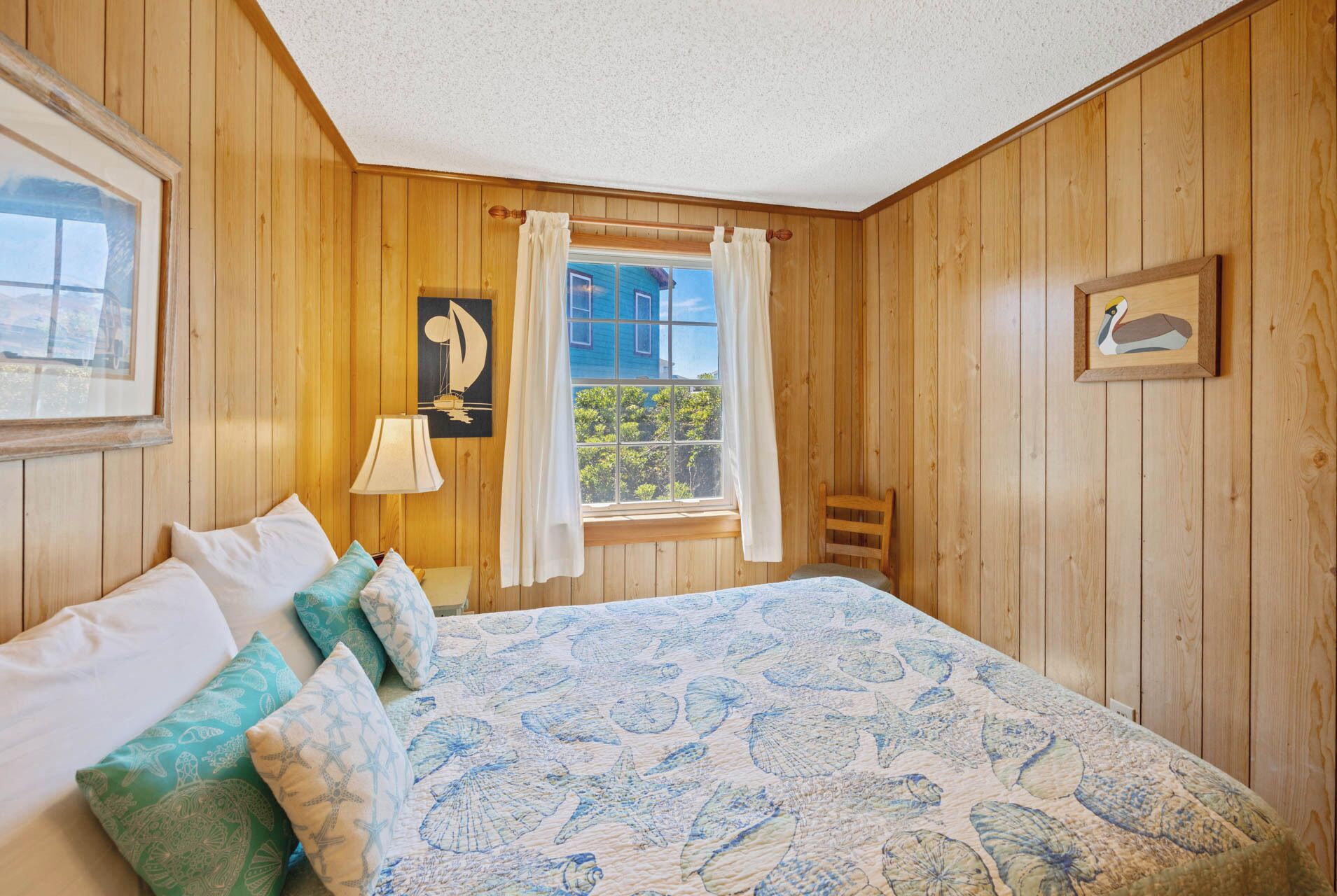 A wooden-paneled room with a bed, a window with curtains, a wall-mounted lamp, and a framed picture.