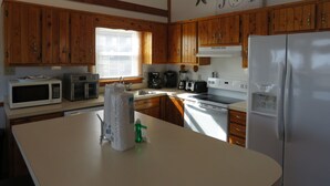 A kitchen with wooden cabinets, a microwave, a toaster, a refrigerator, and a clock on the wall. - Last Minute, low price/Great Ocean view/ Pool/ Ping Pong table/Fenced pet area (Nags Head)