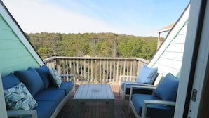 A covered deck with a sofa and chairs, a table, and a view of a forested area. - Last Minute, low price/Great Ocean view/ Pool/ Ping Pong table/Fenced pet area (Nags Head)