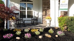A building with a stone facade, a covered porch with chairs, and a flower bed with various flowers. - Great reviews! Available for Masters Tournament (Evans)
