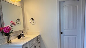 A bathroom with a white vanity, a large mirror, a ring light, and a door with a black knob.