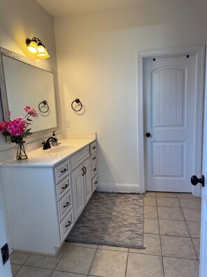 A bathroom with a white vanity, a large mirror, a ring light, and a door with a black knob.