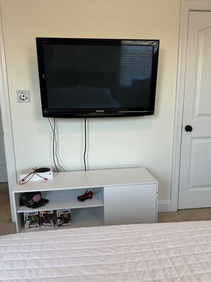 A television mounted on a white wall, with a white entertainment unit below it containing a few toys and a remote control.