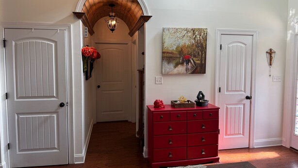 A hallway with white doors, a red dresser, and a painting on the wall.