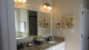 A bathroom with a large mirror, two sinks, a vanity with drawers, and two wall-mounted towel rings.