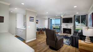 A modern living room with a fireplace, a flat-screen TV, and a dining area with a view of the outdoors. - Modern & Cozy 1-Bedroom with Scenic Walkout Patio – Perfectly Remodeled (Oceanside)