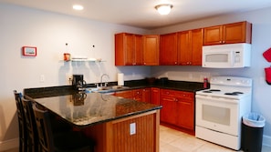 A modern kitchen with wooden cabinets, a granite countertop, a built-in oven, and a microwave. - F2, Downtown St. Augustine, POOL, beaches, spacious, free onsite parking! (Saint Augustine)