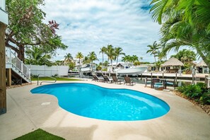 A swimming pool with lounge chairs, a boat dock, and a thatched-roof structure. - P46 - Beautiful updated home on the Gulf side with pool and dock! (Marathon)