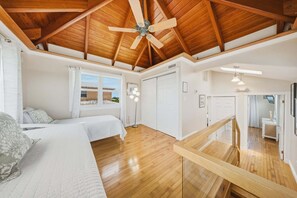 Un dormitorio con techo de madera, una cama, una mesita de noche, una lámpara de pie y vistas al exterior.