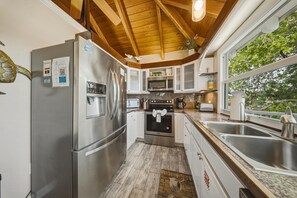 Una cocina con electrodomésticos de acero inoxidable, techo de madera y vistas a árboles.