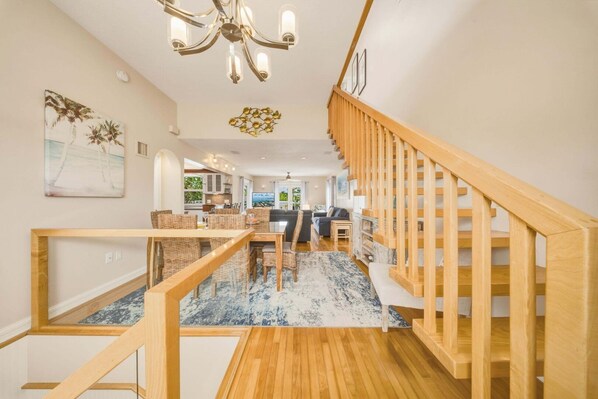 A modern interior with a wooden staircase, a dining area with wicker furniture, and a view through to a kitchen and living space.