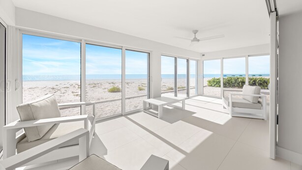 A spacious room with large windows overlooking a beach, white furniture, and a ceiling fan. - Gulf Front Condo! Modern Updated Condo on the Sand ! (Sanibel)